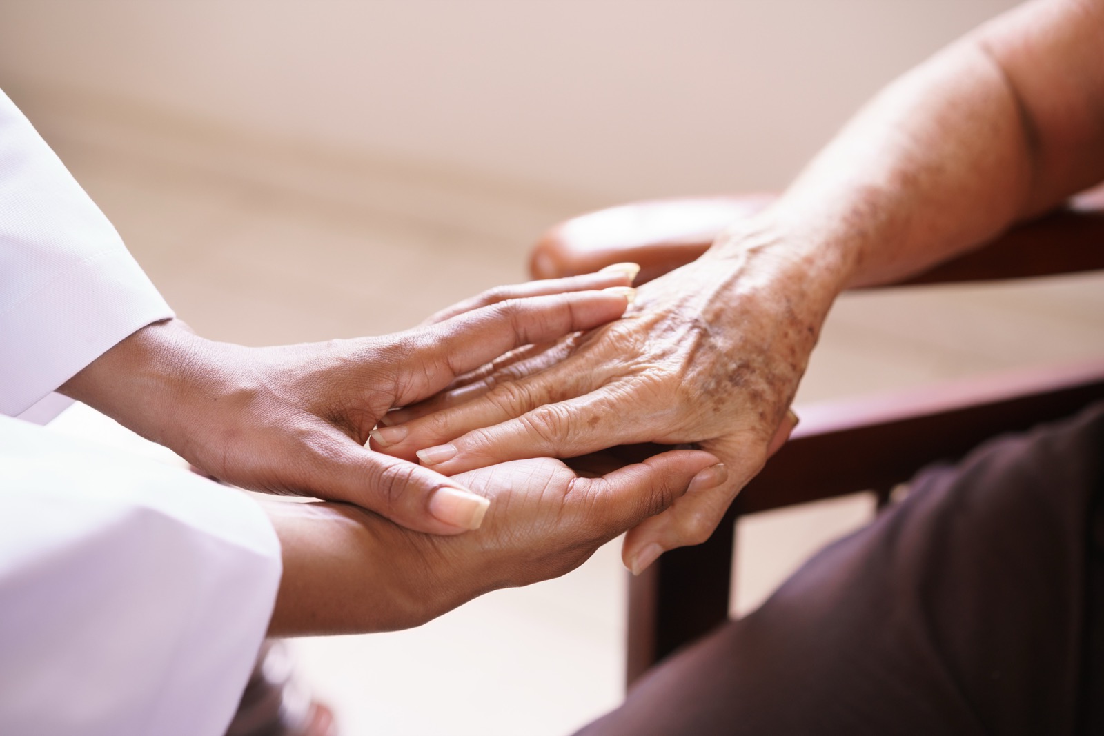 A caregiver's hands cradle an elderly person's weathered hand, a gesture of comfort and reassurance.